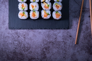 Salmon and avocado maki roll on a slate plate with chopsticks on concrete background. Japanese food. Top view.