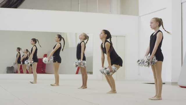 Side view shot of teen and preteen girls with pom-poms jumping together during cheerleading practice