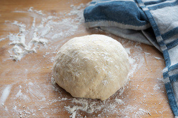 Raw yeast dough for bread or cake ready to rise on a wooden baking board some flour and a blue kitchen towel