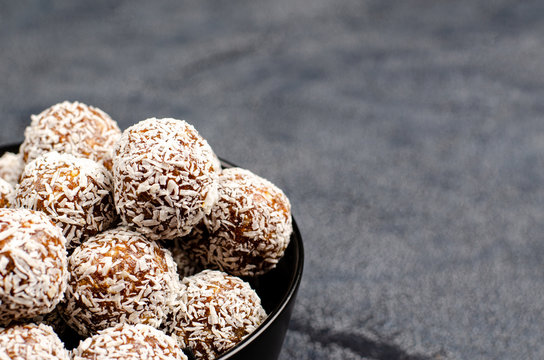 Energy balls from dates, peanuts, honey, oats in a black bowl on a dark background, copy space, flat lay