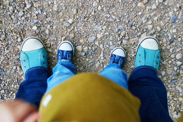 Closeupe of legs of an adult and a toddler in jeans and sneakers