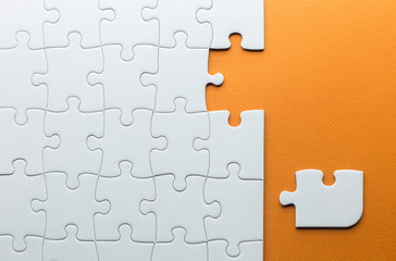puzzle piece that does not fit with the others, white puzzle pieces on a textured orange background