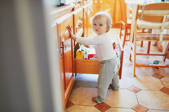 Adorable Toddler Girl At Home, Opening The Drawer In The Kitchen