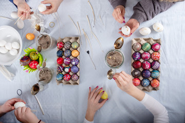 human hands of 4 sorbian women are writing with melting wax on the white surface of the egg on a Table with painted easter eggs.