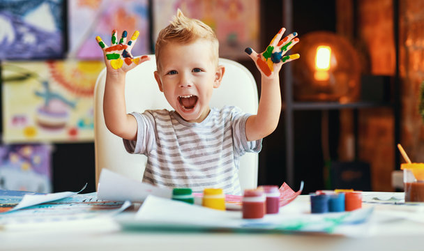 funny child boy draws laughing shows hands dirty with paint