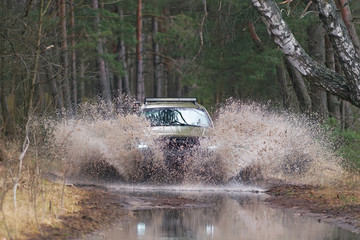 Fototapeta na wymiar Dutch army green mid-size lifted SUV car (4x4 off-road vehicle) driving outdoors on a floody rural road overcoming a water