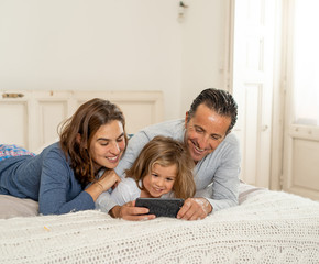 Happy family using mobile smartphone together having fun together in bed