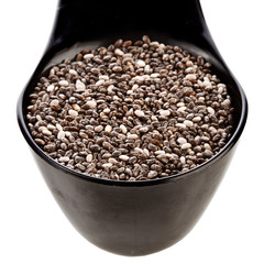 Chia seeds in a black plastic spoon isolated on a white background. Top view.