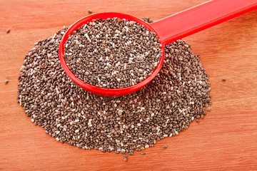Chia seeds in a red spoon on a wooden table.