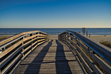 Fototapeta na wymiar Eine einsame Holzbrücke mit Sträuchern an der Seite, die zum Strand führt