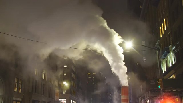 Steam rises and drifts among the rows of buildings along the Fifth Avenue in the night at New York City NY USA during the Christmas Holidays seasons on Dec. 2018.