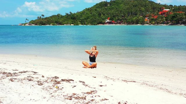 Happy woman with a big smile practicing yoga and meditating on the sandbar in Thailand. Leisure and relaxation, mind relief in nature.