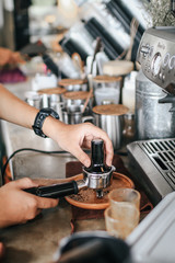 Barista pressing ground coffee into portafilter by tamper to making coffee.Coffee machine preparing fresh coffee. Closeup of filter holder with ground powder on bar coffee maker. and pouring into whit