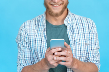 Closeup bearded young man student hipster fun blogger hold use modern smart phone smile screen read text message chat online skype messenger try app isolated blue studio background technology concept,