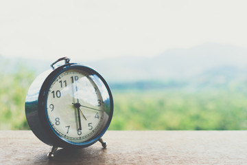 Selective focus of alarm clock on table with nature bokeh mountain background.