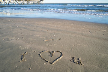 Fototapeta na wymiar ich liebe dich! Ein Herz in Sand gemalt, am Strand in Florida - während goldener Stunde, Meer und Wellen im Hintergrund