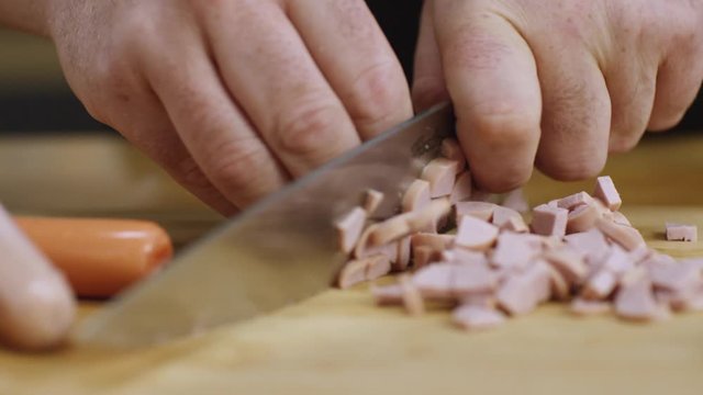 Hands of man cutting sausages on a wooden chopping board with a kitchen knife. Stock footage. Preparing food, close-up view.