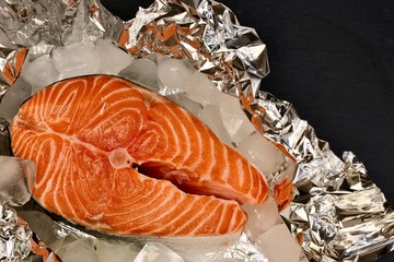 Horizontally placed salmon steak on aluminum foil with ice.