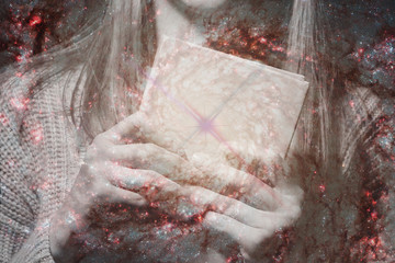 Two female hands holding a magic book on a background of the starry sky.The concept of the spell of...