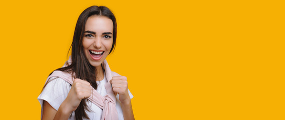 Emotional caucasian girl gesturing fight while shouting and posing on yellow background with blank...