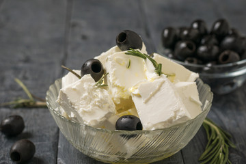 Glass bowl with slices of feta cheese and olives on a wooden table.