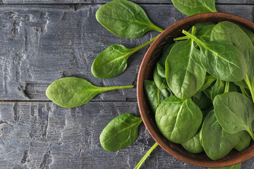 Fresh spinach leaves are scattered on the table and in a clay bowl. Food for fitness. The view from...