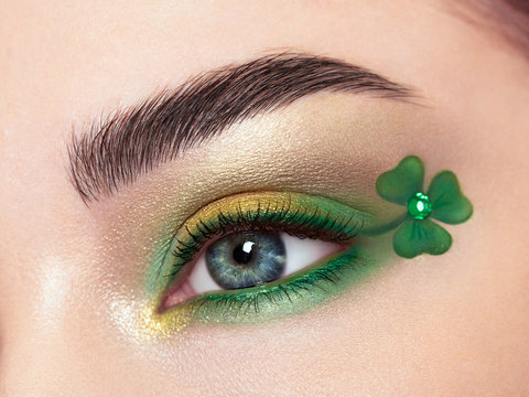 Conceptual photo of St. Patrick's Day. The eye of the young beautiful woman with bright green shadows and expressive eyebrows. Shamrock patterns. Holiday makeup