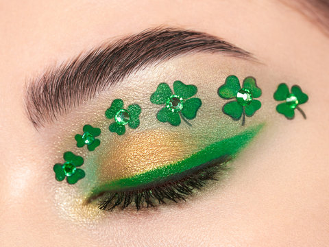 Conceptual photo of St. Patrick's Day. The eye of the young beautiful woman with bright green shadows and expressive eyebrows. Shamrock patterns. Holiday makeup