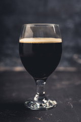Freshly brewed dark beer on the black rustic background. Selective focus. Shallow depth of field.