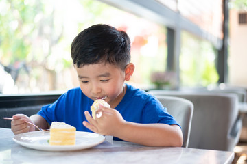 Asian boy eating cake in bakery shop or cafe.