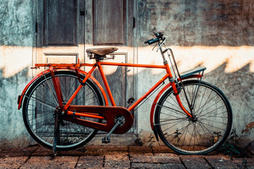 Fototapeta na wymiar Red orange vintage bicycle parked in front of an old wall.