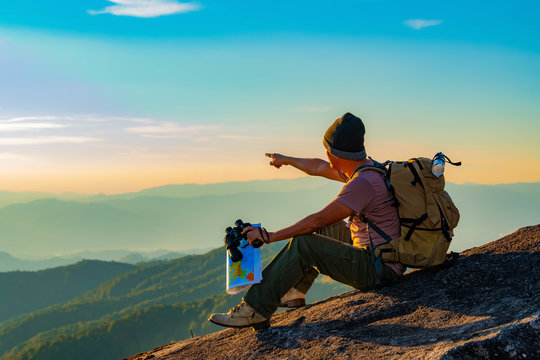 The young man with a lifted backpack looked in binoculars sitting on the top of the mountain, enjoying the beautiful landscape view of the mountains above the clouds. sport © EKKAPON