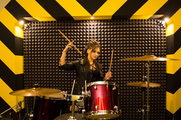 young beautiful tattooed girl in a leather jacket plays drums in a recording Studio on the bright...