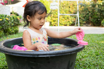 Cute little girl playing in round plastic wash basin during hot weather.