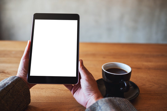 Mockup image of woman holding black tablet pc with blank white screen with coffee cup on wooden table