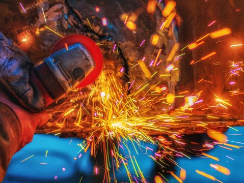 worker grinding cutting metal sheet with grinder machine overwrites the master of welding seams angle grinder and sparks. Electric grinder in the industrial workshop.