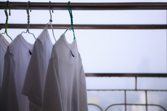 White T Shirts hung on Cloth hangers on Cloth Line at the balcony of residential building in a rainy day with blurry city view background, cannot dry clothes on bad day. City Life, Living on High Rise