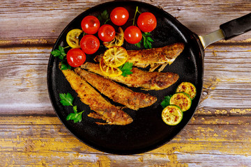 Fried whole capelin fish in a pan on a wooden background.
