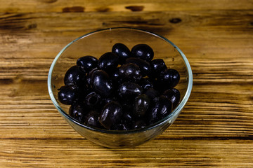 Glass bowl with black olives on wooden table