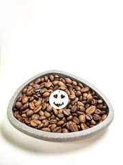 Roasted coffee beans in a bowl and a smiley face on a white background.