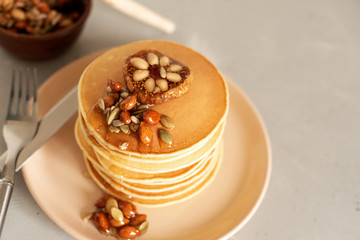 Stack of delicious pancakes with chocolate, honey, nuts and slices of banana on plate and napkin on wooden background