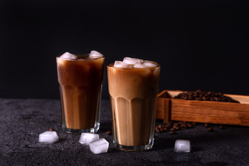 Iced coffee in a tall glass with cream poured over. Wood background. Low key.