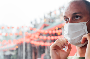 Man putting on a mask next to a Chinese temple. Virus concept