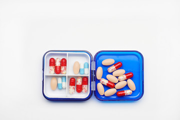 many tablets and capsules in a plastic container on a white background.