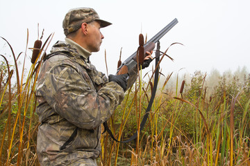 a hunter with a gun stands in a thicket of cattails