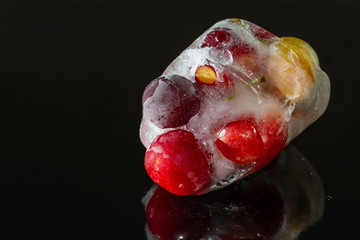 Cherry plum frozen in ice with reflection on dark background with water drops. Cracked ice. Closeup, selective focus