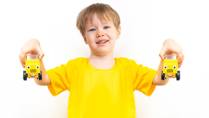 Two yellow cars with painted eyes and smile in hands of Little European happy happy child boy. Kid...