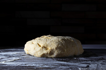 Fresh raw dough for making bread, pasta or pizza on a dark wooden table on a black background. Copy space