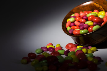 Multi-colored sweets in a wooden bowl on a dark background