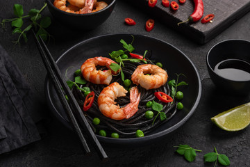 Black spaghetti. Cuttlefish ink pasta with shrimp, green peas and chili in a black plate. Seafood noodles. Selective focus